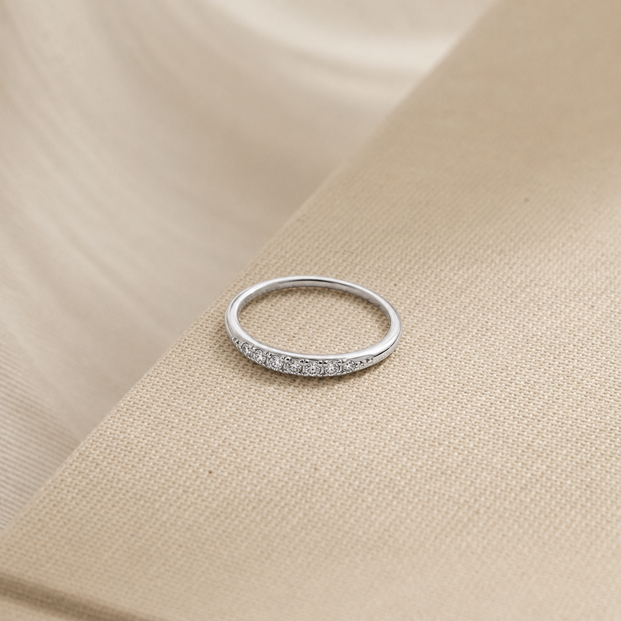 Silver ring with small diamonds on a beige fabric background